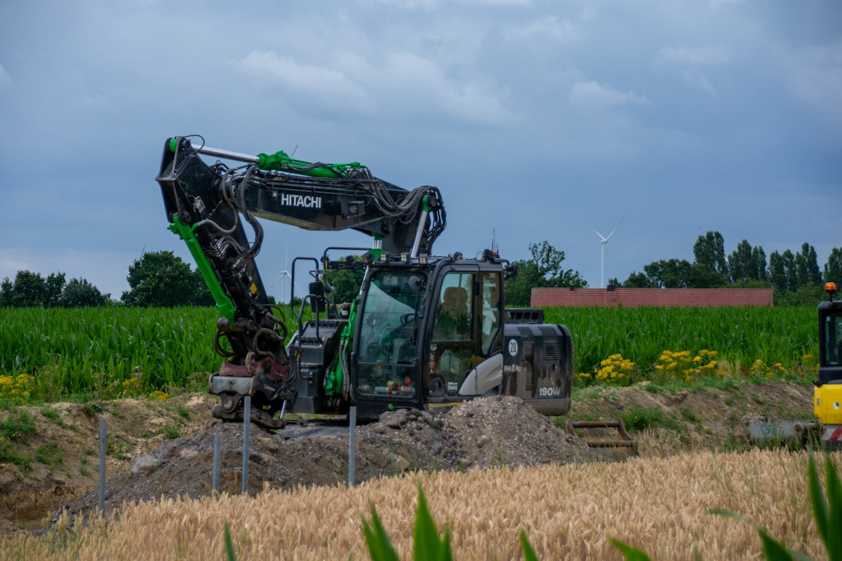 A large excavator digging dirt between green and golden fields.