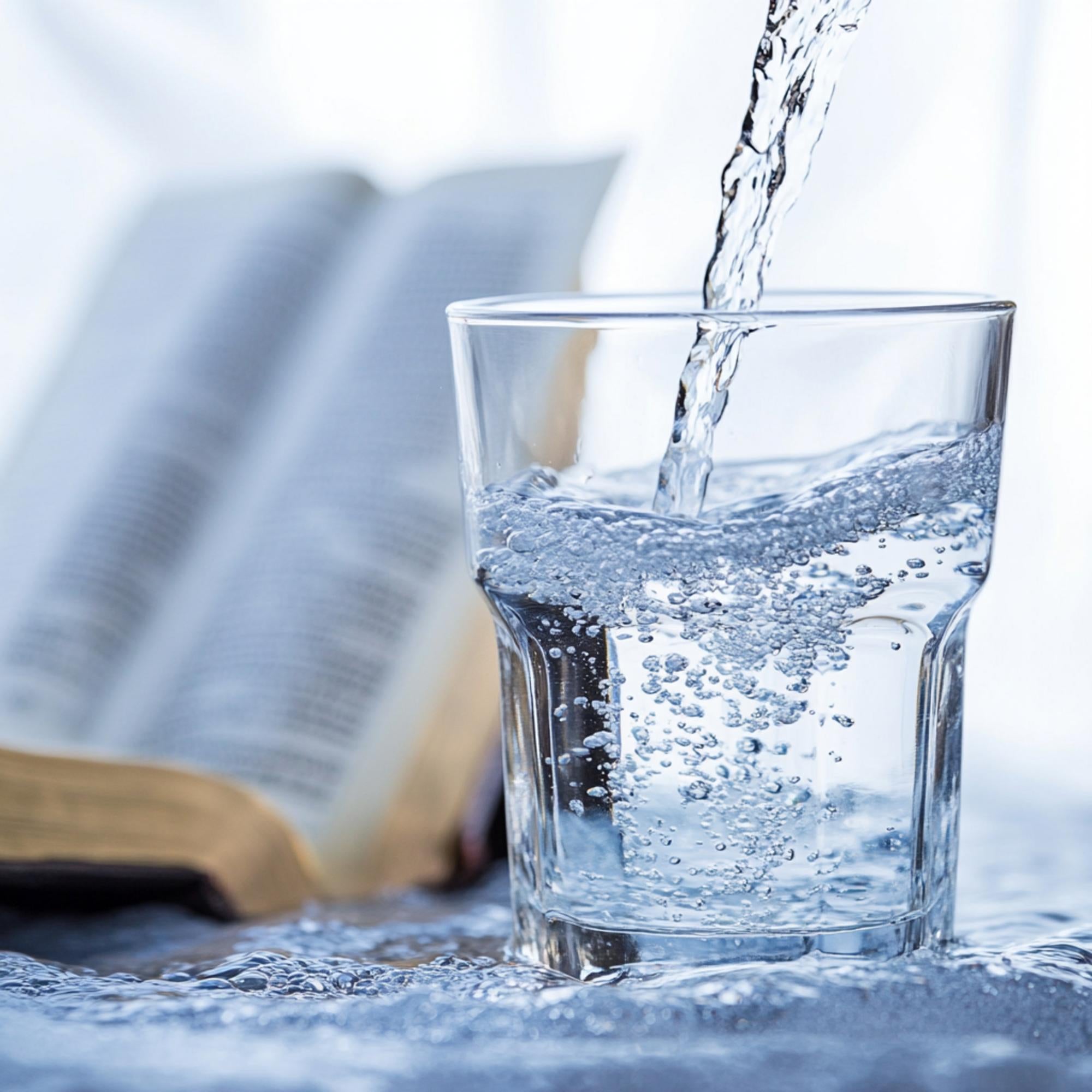 Glas wordt gevuld met helder drinkwater op tafel naast open boek – symbool voor zuiverheid en gezondheid met kraanwaterfilter