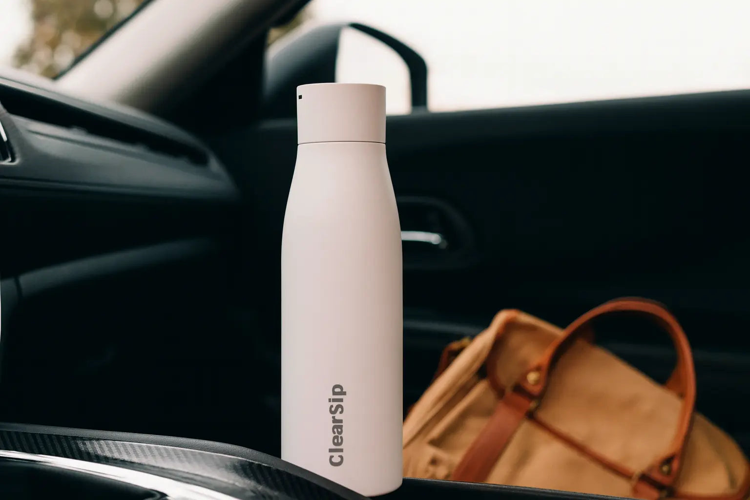 sneeuwwitte herbruikbare ClearSip waterfles in auto naast tas als duurzame drinkfles voor onderweg