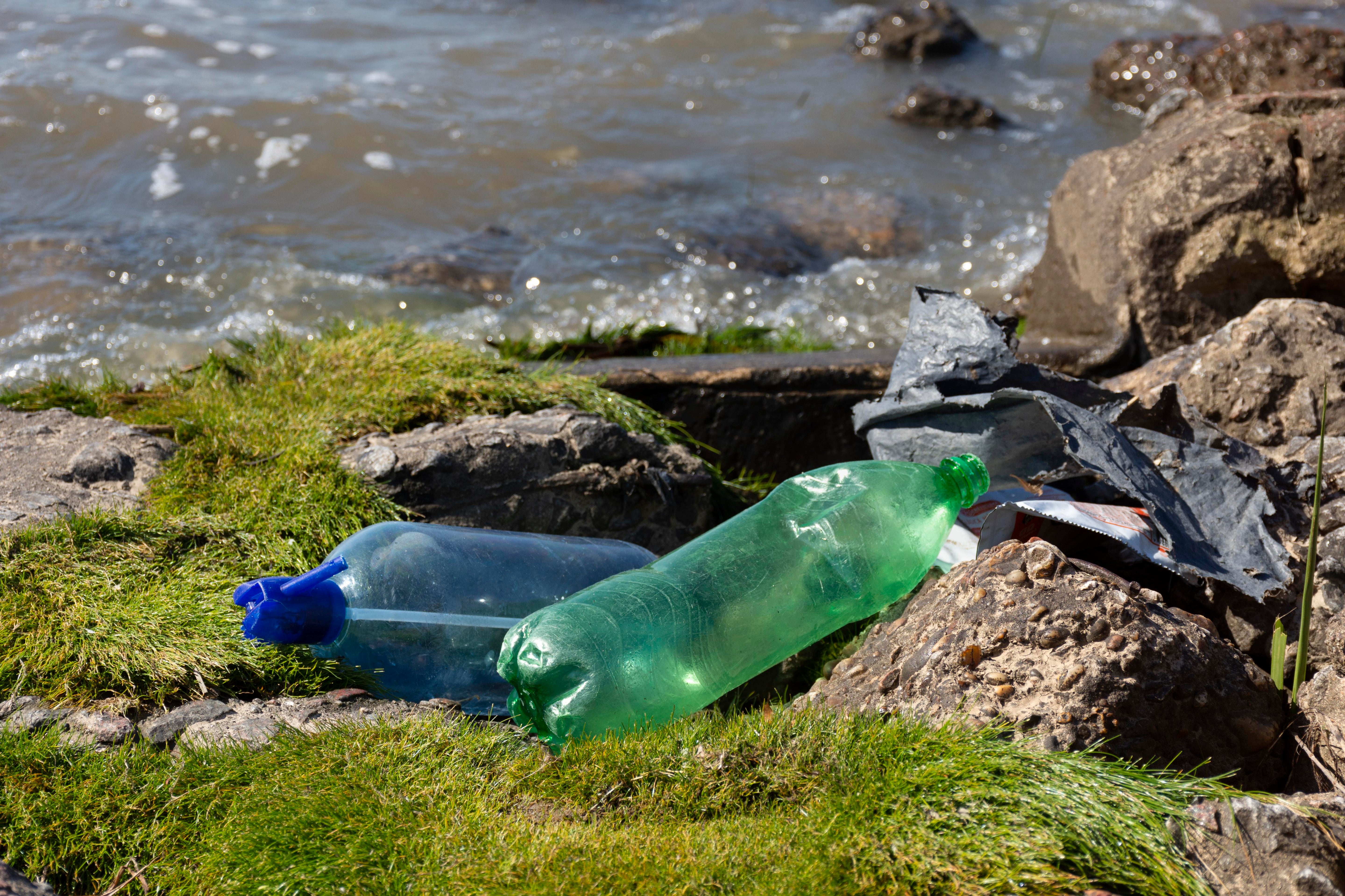 Plastic flessen en afval op de oever bij het water, vervuiling van natuur en milieu door zwerfafval